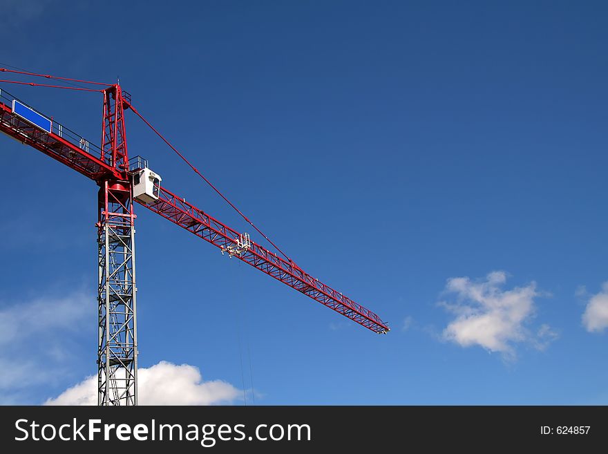 Red construction crane on blue sky background with some white clouds.