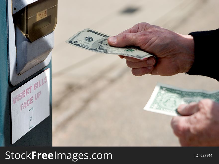 An older gentleman feeds a five dollar bill into the machine. An older gentleman feeds a five dollar bill into the machine.