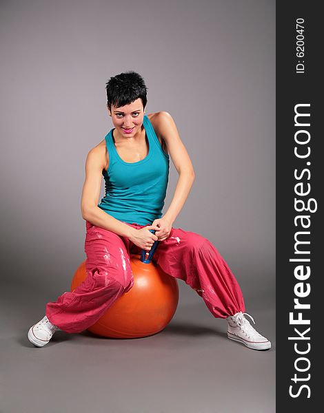 Young woman in sportswear sits on a orange ball