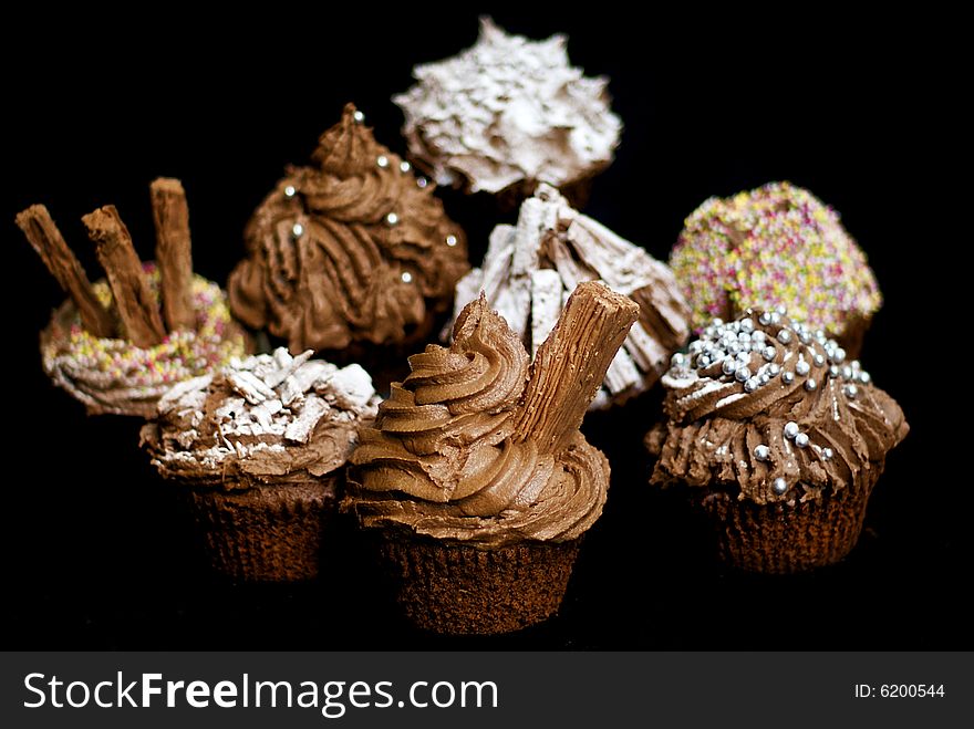 Cup cakes/Muffins suitable for a birthday card or celebration card.chocolate fondant icing and silver balls, icing sugar, flakes and sprinkles, shallow depth of field to isolate foremost cake. Cup cakes/Muffins suitable for a birthday card or celebration card.chocolate fondant icing and silver balls, icing sugar, flakes and sprinkles, shallow depth of field to isolate foremost cake