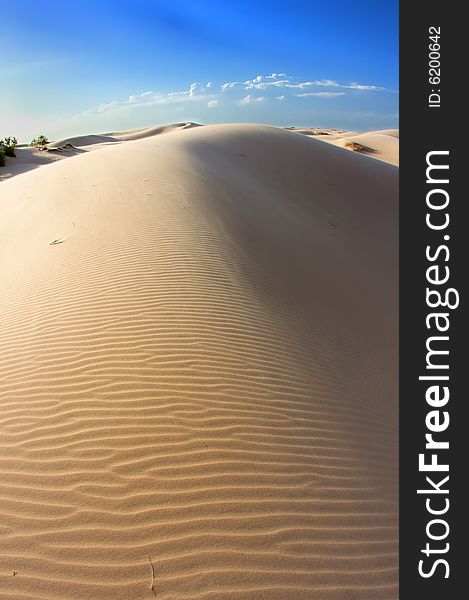 An image of windswept sand dunes on a blue sky. An image of windswept sand dunes on a blue sky