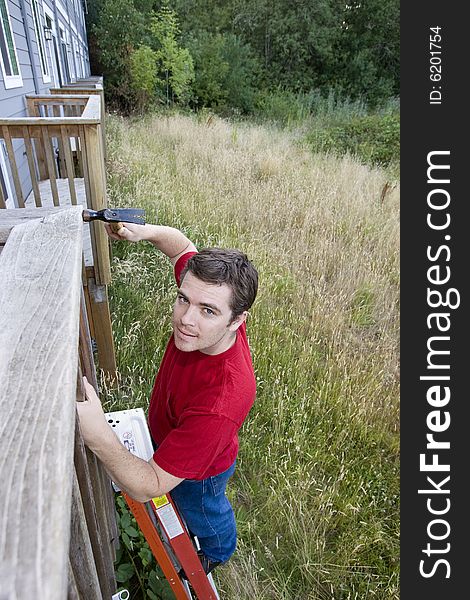 Man standing on a ladder hammering a porch. Vertically framed photo. Man standing on a ladder hammering a porch. Vertically framed photo.