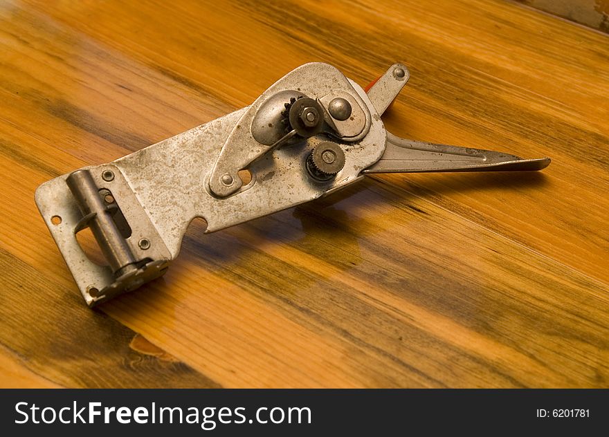 Old can opener placed on wood counter.