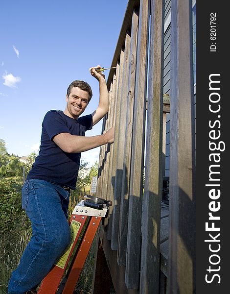 Happy man on a ladder repairing siding of a house with a screwdriver. Vertically framed photo. Happy man on a ladder repairing siding of a house with a screwdriver. Vertically framed photo.