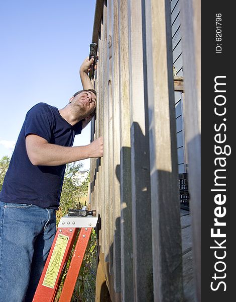 Man on a ladder repairing siding of a house with a wrench while looking up in the sky. Vertically framed photo. Man on a ladder repairing siding of a house with a wrench while looking up in the sky. Vertically framed photo.
