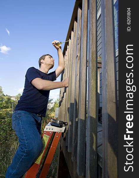 Man on a ladder repairing siding of a house with a screwdriver. Vertically framed photo. Man on a ladder repairing siding of a house with a screwdriver. Vertically framed photo.