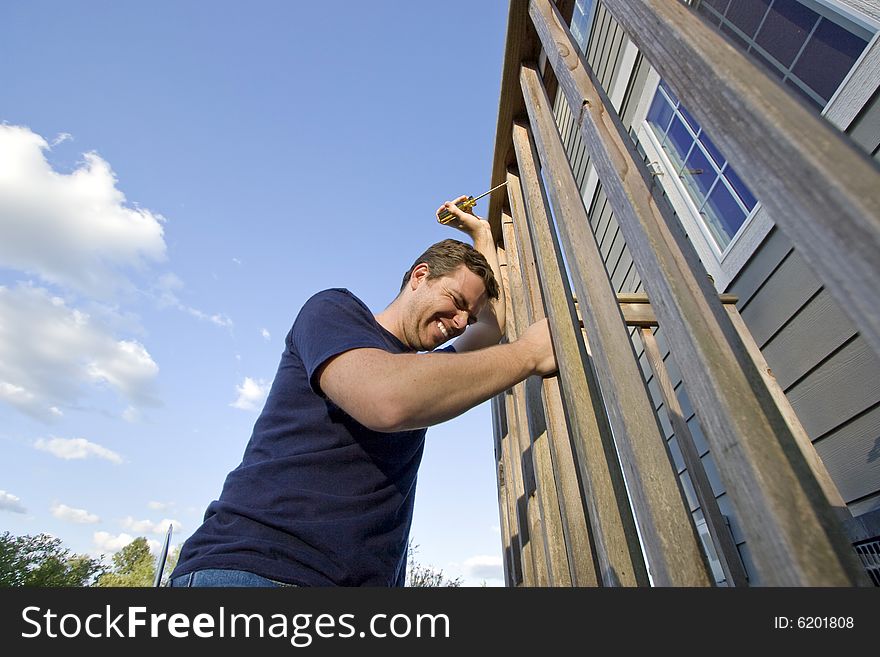 Frowning man fixing the siding on a house with a screwdriver. Horizontally framed photo. Frowning man fixing the siding on a house with a screwdriver. Horizontally framed photo.