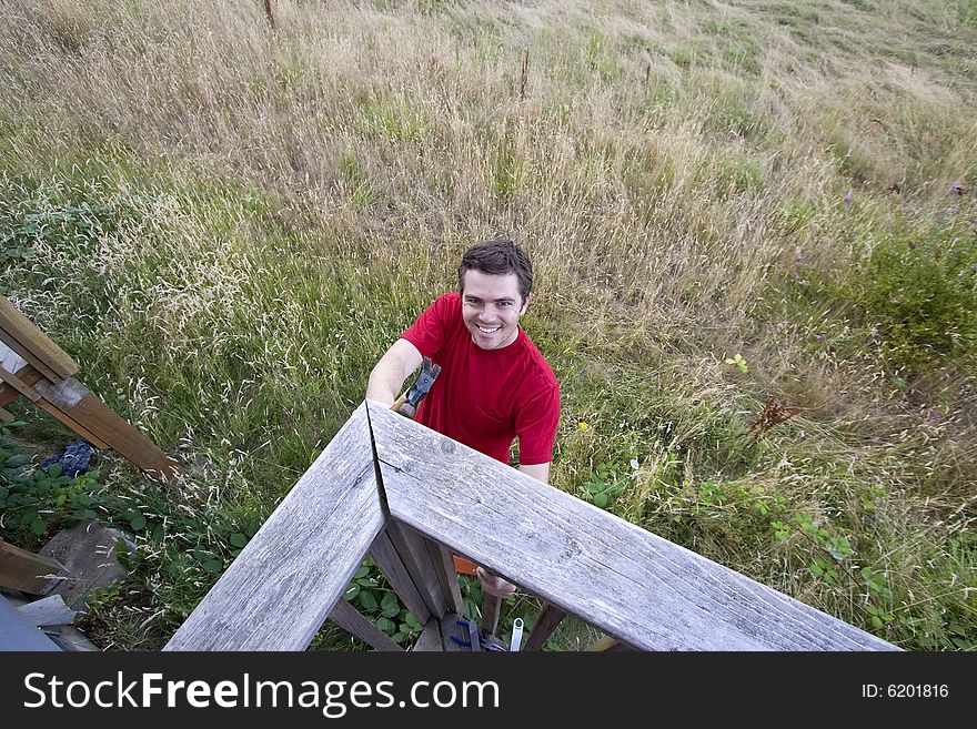 Aerial view of  a frowning man  on ladder hammering a porch. Horizontally framed photo. Aerial view of  a frowning man  on ladder hammering a porch. Horizontally framed photo.