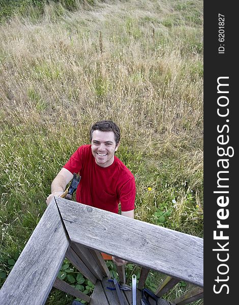 Aerial view of  a smiling man  on ladder hammering a porch. Vertically framed photo. Aerial view of  a smiling man  on ladder hammering a porch. Vertically framed photo.