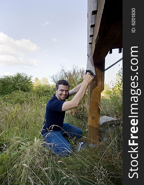 Man fixing a beam on a house with a saw. He looks happy and is smiling. Vertically framed photo. Man fixing a beam on a house with a saw. He looks happy and is smiling. Vertically framed photo.