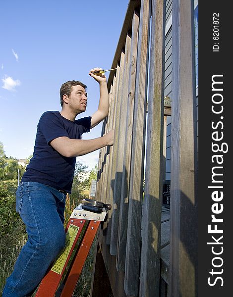 Man on ladder fixing the siding on a house with a screwdriver. Vertically framed photo. Man on ladder fixing the siding on a house with a screwdriver. Vertically framed photo.