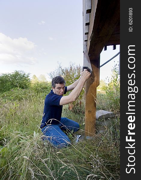 Man fixing a beam on a house with a saw. He looks unhappy . Vertically framed photo. Man fixing a beam on a house with a saw. He looks unhappy . Vertically framed photo.