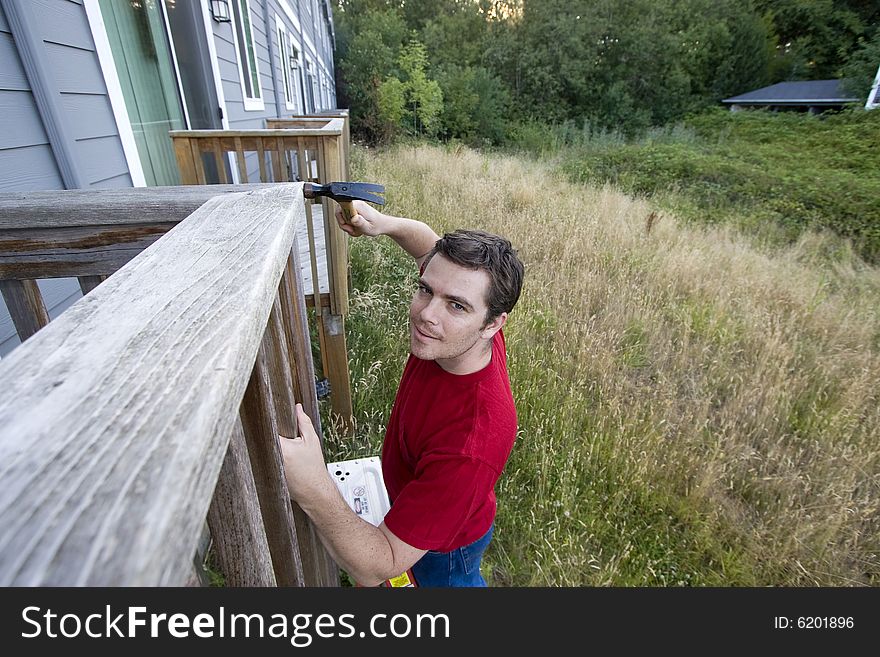 Man standing on a ladder hammering a porch. Horizontally framed photo. Man standing on a ladder hammering a porch. Horizontally framed photo.