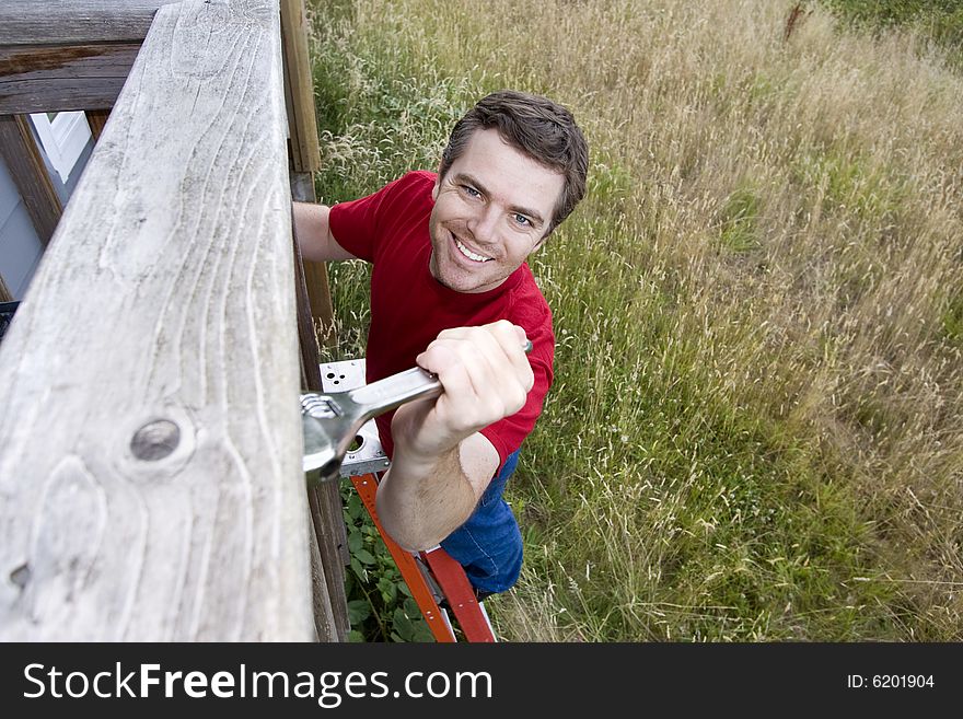 Happy man standing on a ladder fixing a porch with a wrench. Horizontally framed photo. Happy man standing on a ladder fixing a porch with a wrench. Horizontally framed photo.