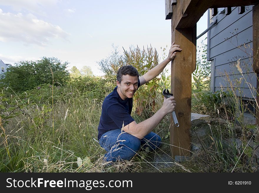Smiling man fixing a beam on a house with a wrench. Horizontally framed photo. Smiling man fixing a beam on a house with a wrench. Horizontally framed photo.