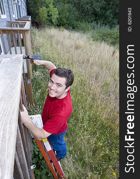 Man standing on a ladder hammering a porch. Vertically framed photo. Man standing on a ladder hammering a porch. Vertically framed photo.