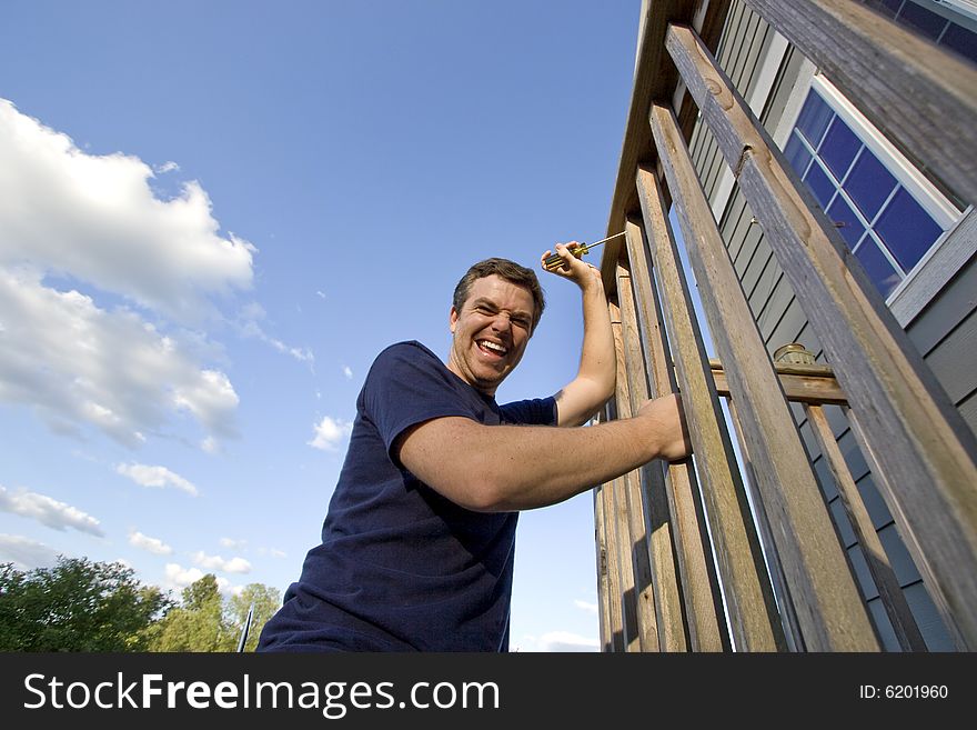 Smiling man fixing the siding on a house with a screwdriver. Horizontally framed photo. Smiling man fixing the siding on a house with a screwdriver. Horizontally framed photo.