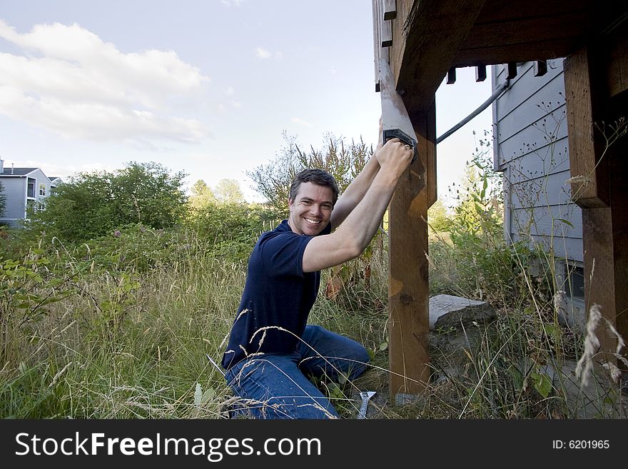 Man fixing a beam on a house with a saw. He looks happy and is smiling. Horizontally framed photo. Man fixing a beam on a house with a saw. He looks happy and is smiling. Horizontally framed photo.