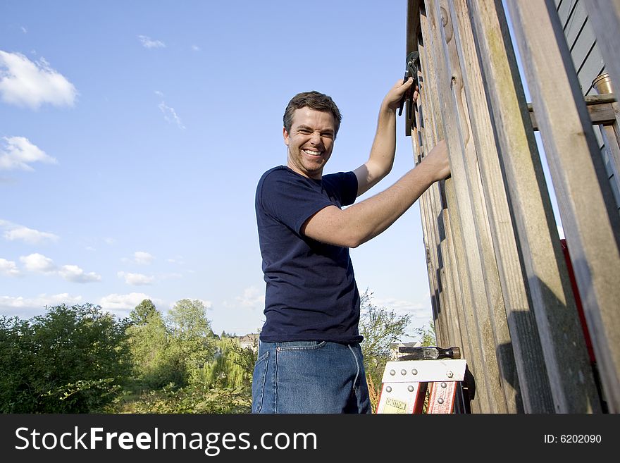 Smiling man on a ladder repairing siding of a house with a wrench. Horizontally framed photo. Smiling man on a ladder repairing siding of a house with a wrench. Horizontally framed photo.