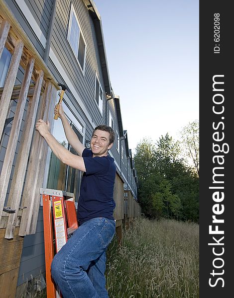 Smiling man on ladder hammering a porch. Vertically framed photo. Smiling man on ladder hammering a porch. Vertically framed photo.