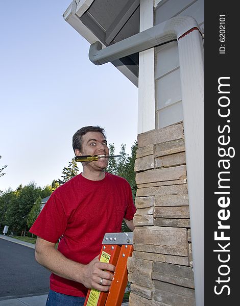 Man on a ladder against a house with a screwdriver in his mouth and a crazy look on his face. Vertically framed photo. Man on a ladder against a house with a screwdriver in his mouth and a crazy look on his face. Vertically framed photo