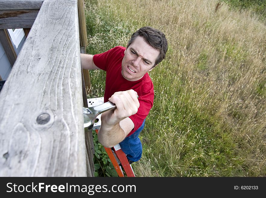 Frustrated man standing on a ladder fixing a porch with a wrench. Horizontally framed photo. Frustrated man standing on a ladder fixing a porch with a wrench. Horizontally framed photo.