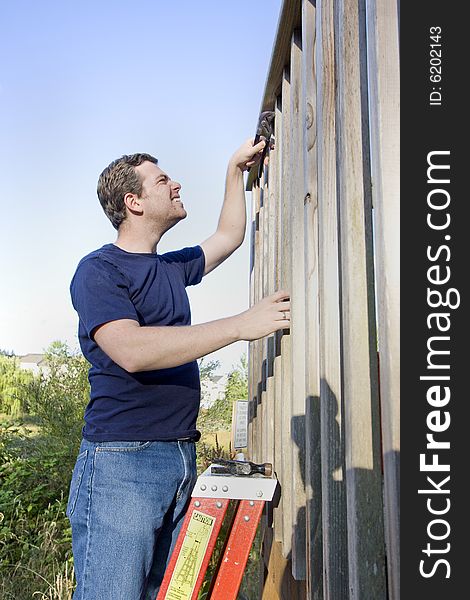 Man on a ladder concentrates while repairing siding of a house with a wrench. Vertically framed photo. Man on a ladder concentrates while repairing siding of a house with a wrench. Vertically framed photo.