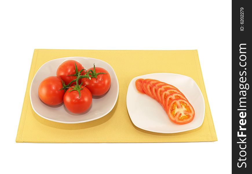 Whole and sliced tomato on white plates on yellow place mat. Whole and sliced tomato on white plates on yellow place mat