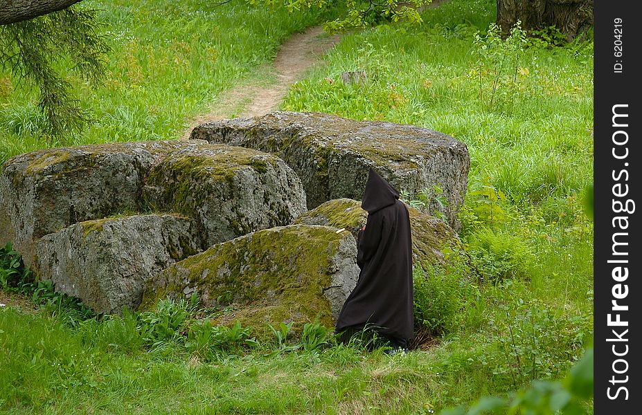 Figure in a black cloak next to enormous stone in a park