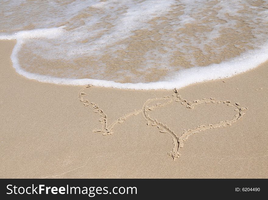 Two hearts drawn in sand on a beach, almost covered by a wave. End of summer love. Two hearts drawn in sand on a beach, almost covered by a wave. End of summer love.