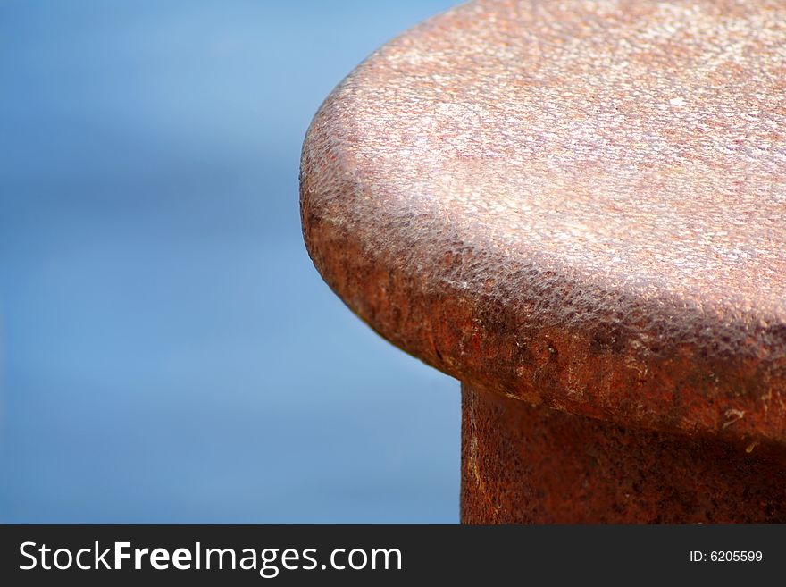 Rusty bollard,closeup, in front of a water background