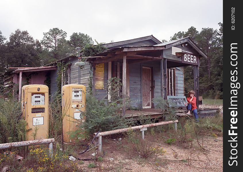 Old Gas Station with sad woman sitting on the porch steps with two yellow gas pumps out front. Old Gas Station with sad woman sitting on the porch steps with two yellow gas pumps out front.