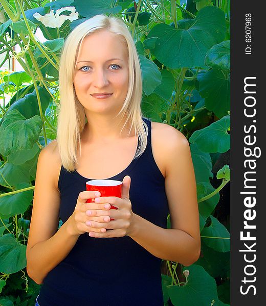 Young beautiful woman with a cup in the morning in a summer garden. Young beautiful woman with a cup in the morning in a summer garden.