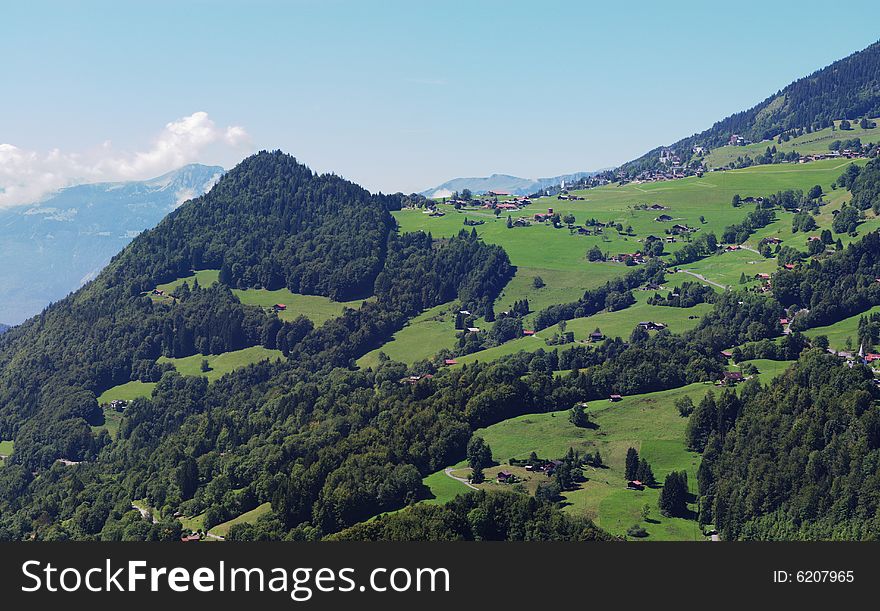 Summer rural landscape view on green Alps mountains, trees, slopes, and detached houses. Alps, Switzerland, europe. Summer rural landscape view on green Alps mountains, trees, slopes, and detached houses. Alps, Switzerland, europe.