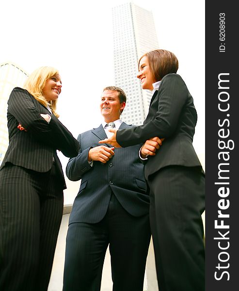 Three business people discuss as a team outdoor with tall downtown building on the background. Three business people discuss as a team outdoor with tall downtown building on the background