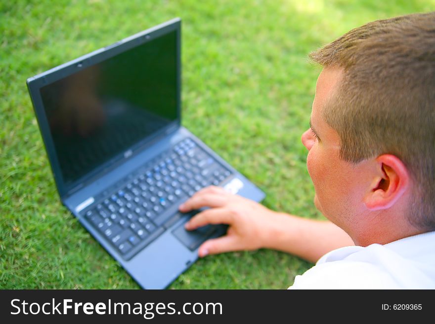 Handsome caucasian man using computer outdoor in grassy park. Handsome caucasian man using computer outdoor in grassy park
