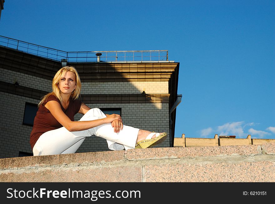 Young blond woman in white jeans sitting on parapet. Young blond woman in white jeans sitting on parapet