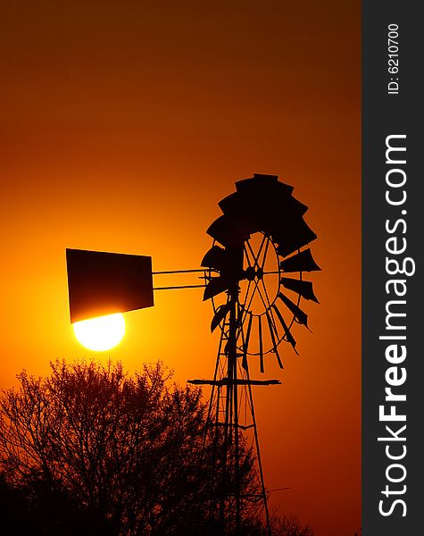 Old windpumpwith sun directly behind it at sunset giving off red glow