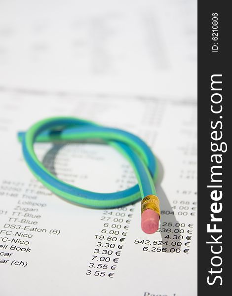 A green and blue striped rubber pencil tied in knot sitting on accounting printout. A green and blue striped rubber pencil tied in knot sitting on accounting printout