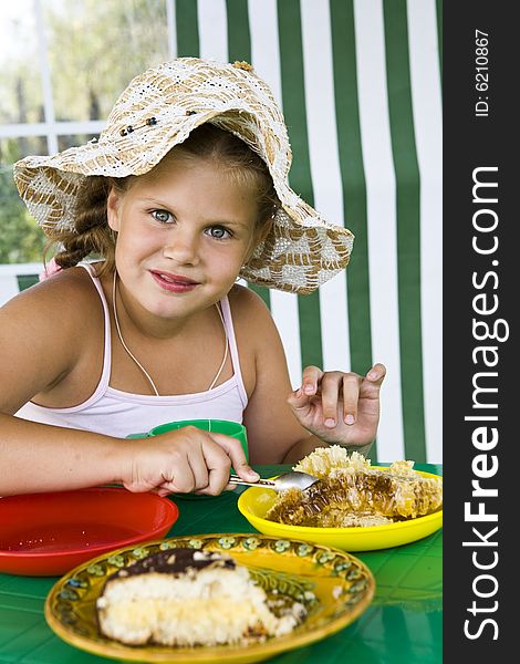 Little girl in big hat eats sweets and drinks tea