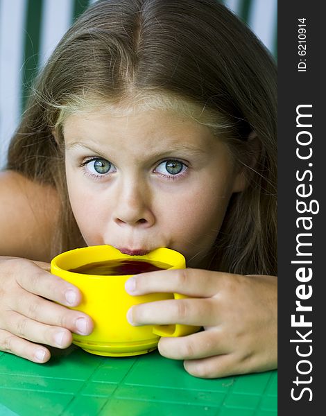 Little blond girl with yellow cup of tea in her hands