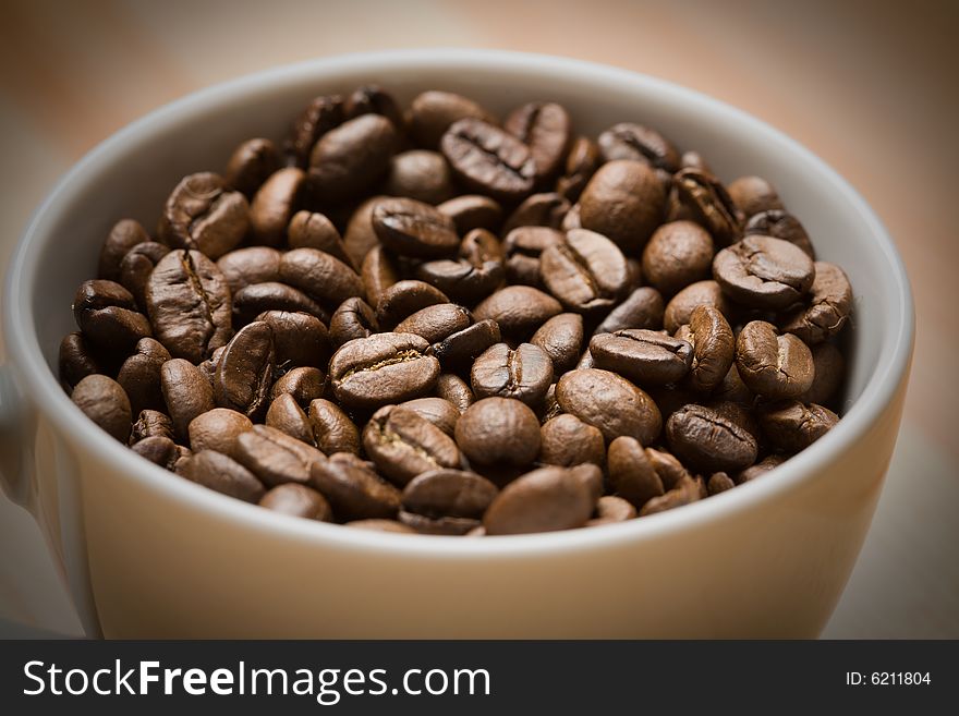 Cup with freshly roasted coffee beans. Light vignetting on the corners