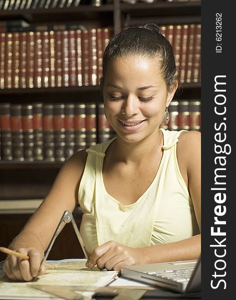 Student smiles as she works with a protractor in an office surrounded by books. Vertically framed photo. Student smiles as she works with a protractor in an office surrounded by books. Vertically framed photo.