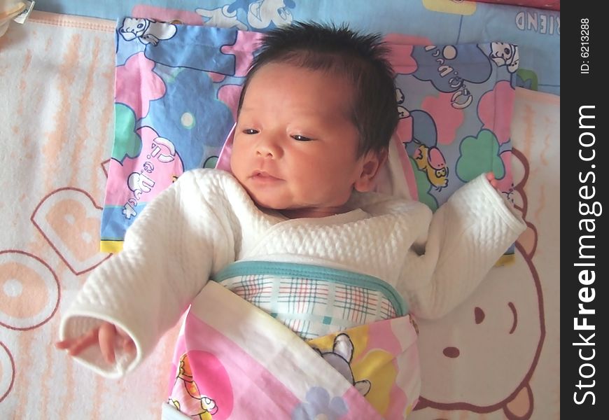 A Chinese infant is waving her hand on the bed. A Chinese infant is waving her hand on the bed