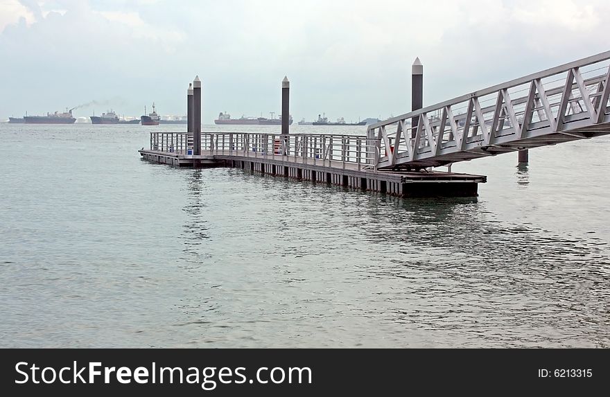 A floating pier linked by a suspended walkway against a busy shipping horizon