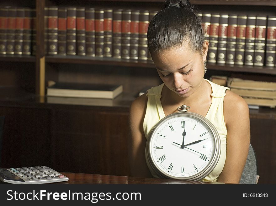Girl in office with books looking at a clock. Horizontally framed photo. Girl in office with books looking at a clock. Horizontally framed photo.
