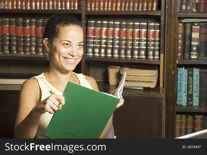 Smiling student reading a book while seated at a desk in an office surrounded by books. Horizontally framed photo. Smiling student reading a book while seated at a desk in an office surrounded by books. Horizontally framed photo.