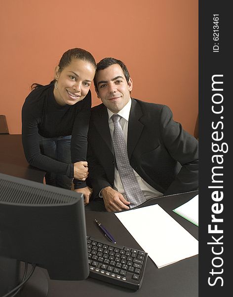 Businessman and woman smile with their heads touching as they work at a desk with a computer. Vertically framed photograph. Businessman and woman smile with their heads touching as they work at a desk with a computer. Vertically framed photograph.