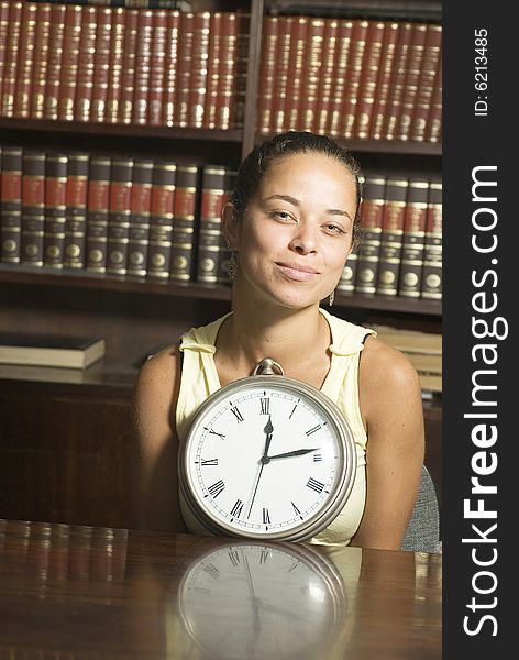 Woman in office smiling holding clock. Vertically framed photo. Woman in office smiling holding clock. Vertically framed photo.