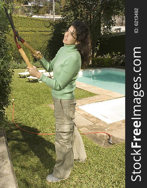 Woman cuts shrubs with trimmers. She is smiling and working in a yard. Vertically framed photo. Woman cuts shrubs with trimmers. She is smiling and working in a yard. Vertically framed photo.